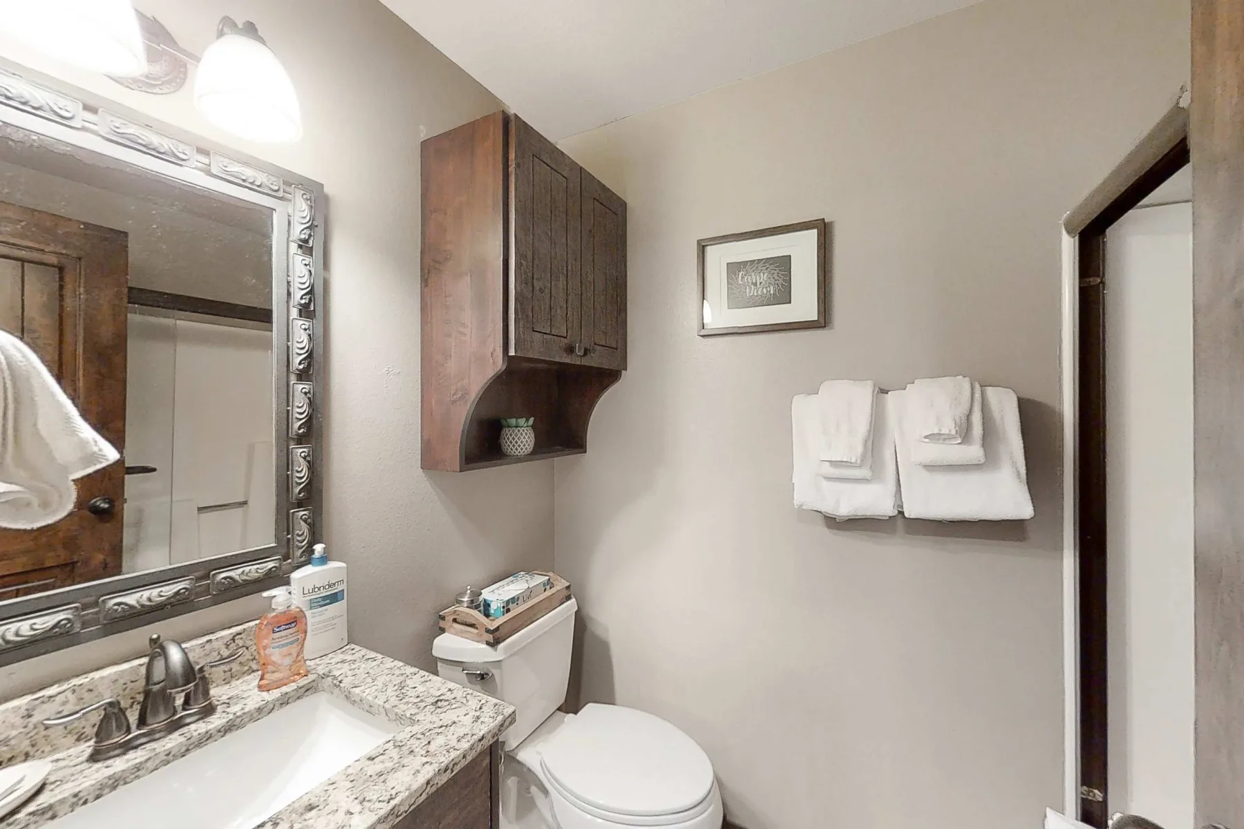 Un lavabo y un inodoro están bajo un armario de pared, con toallas colgadas cerca.