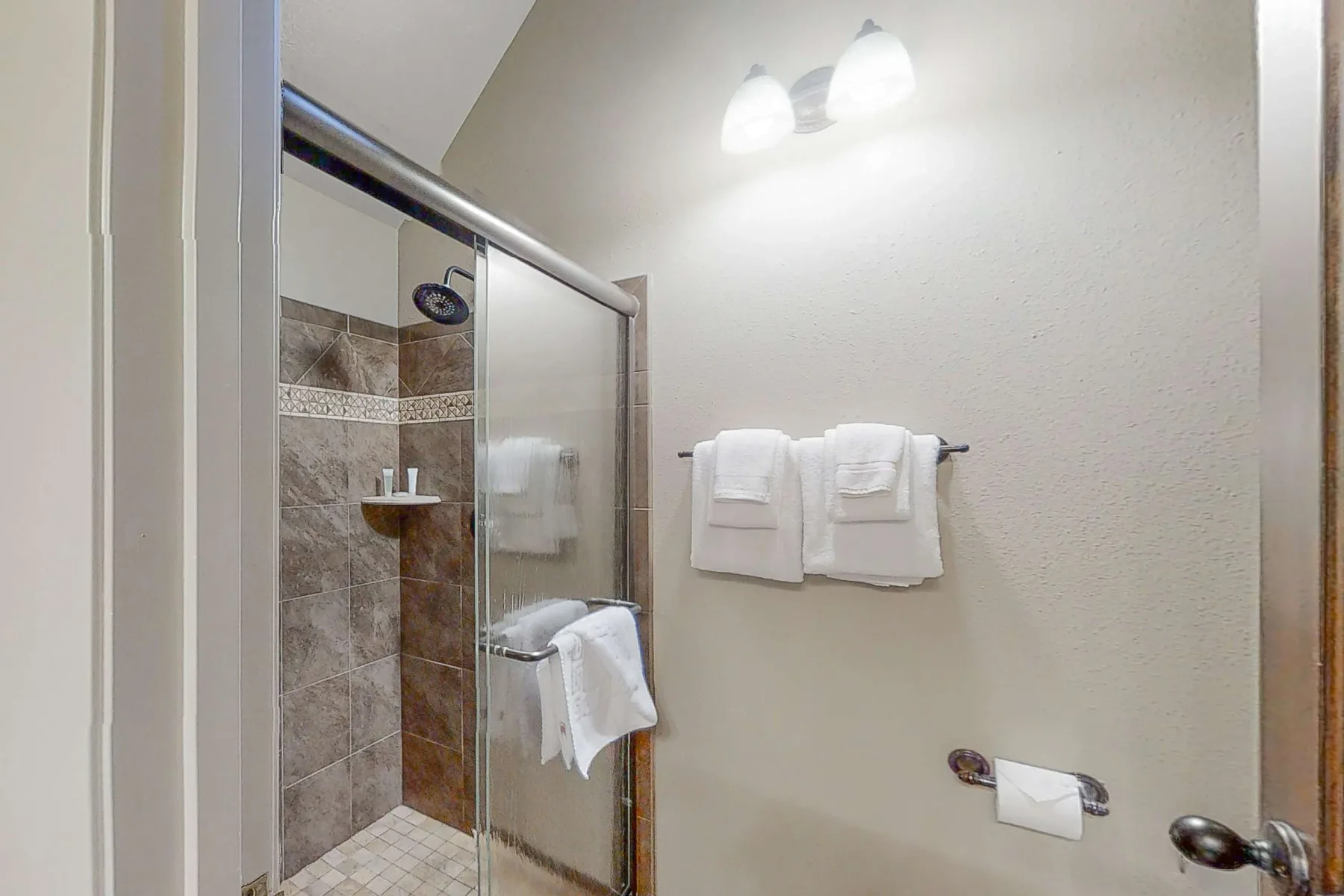 Un baño con una ducha de vidrio y toallas blancas colgadas en la pared.
