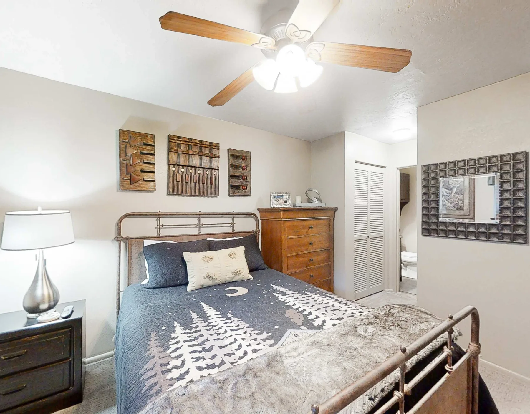 Un dormitorio con una cama de metal, ropa de cama estampada y muebles de madera.