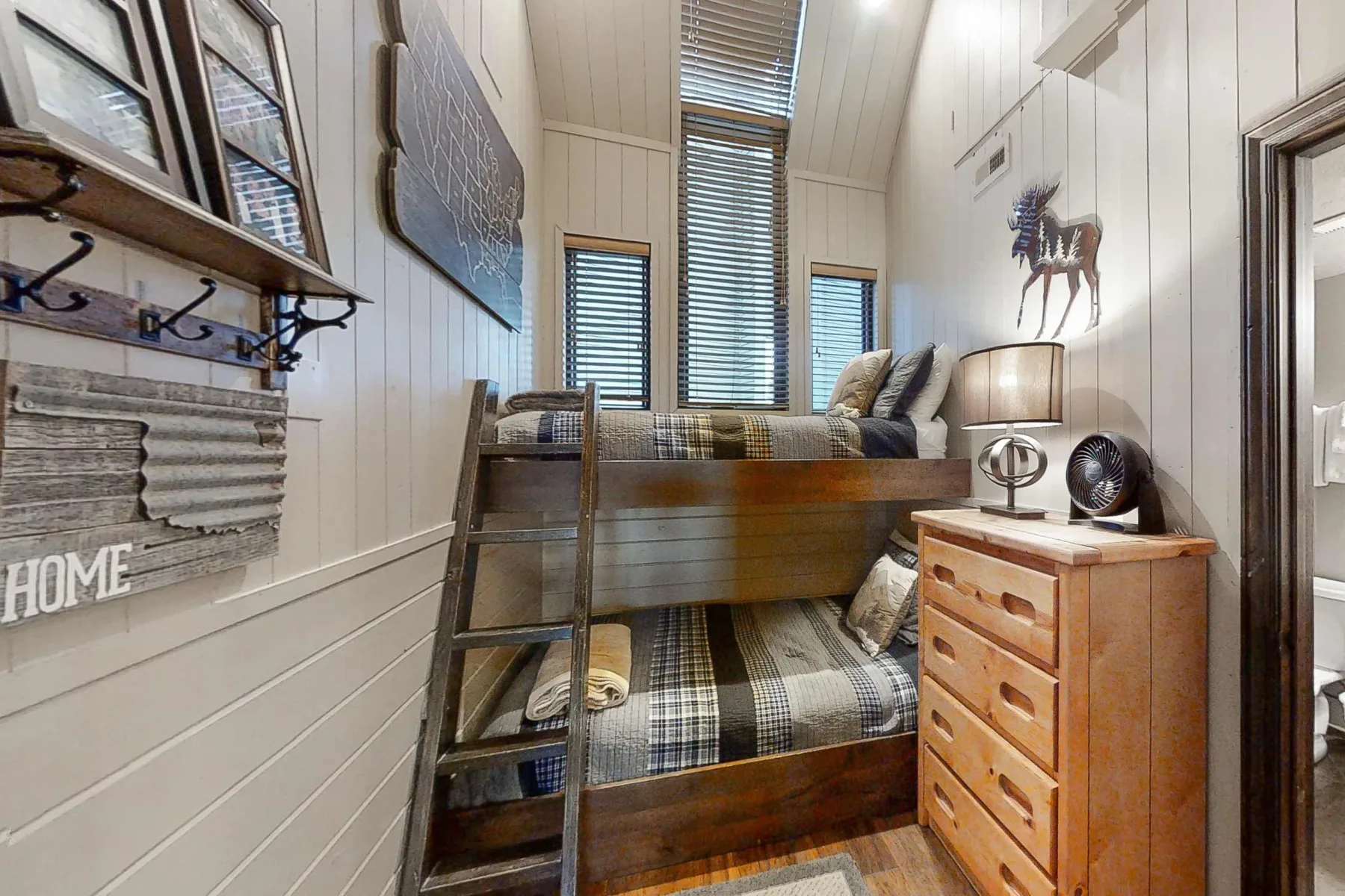 Un dormitorio compacto con una litera de madera, ropa de cama a cuadros y una cómoda.