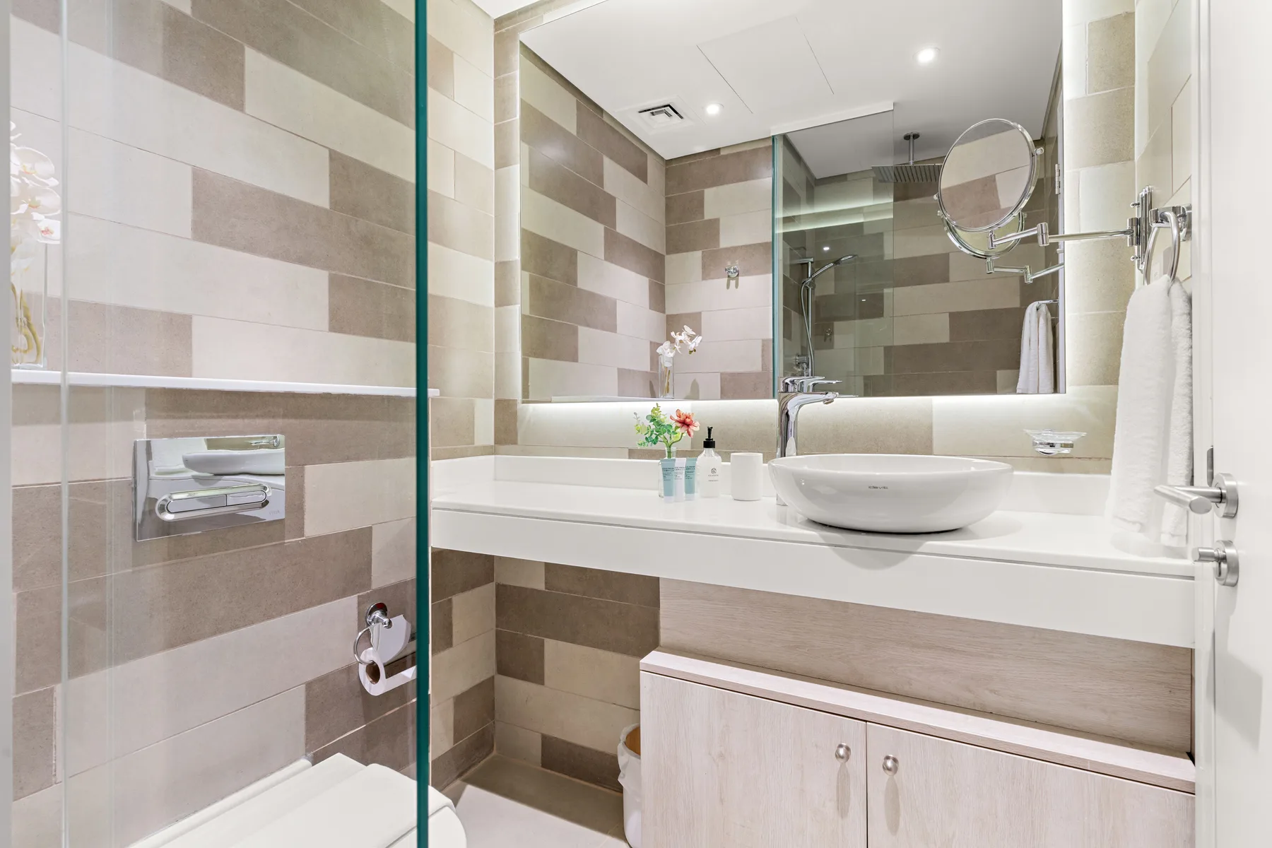 Baño con azulejos, ducha de vidrio, lavabo y espejo amplio.