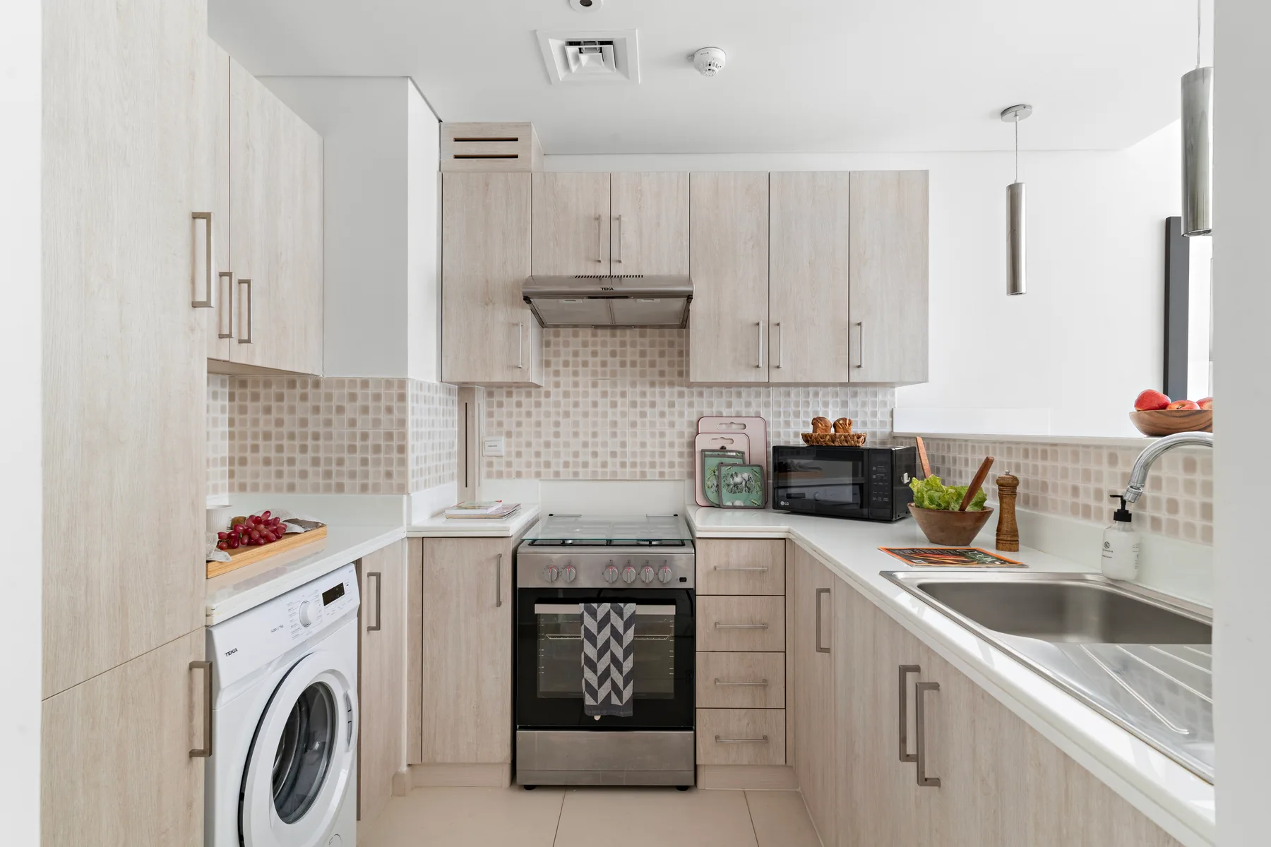 Una cocina luminosa con gabinetes claros, una estufa y una lavadora.