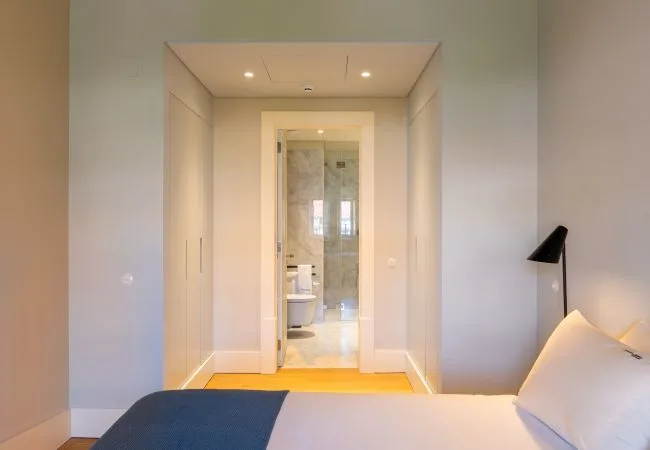 A bedroom with a bed beside a hallway leading to a bathroom.