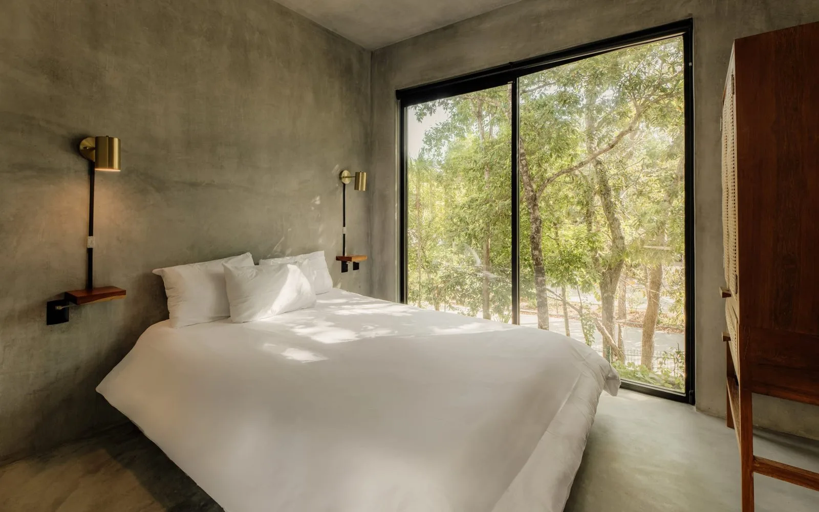 Un dormitorio con una cama blanca junto a una ventana grande con vista a los árboles.