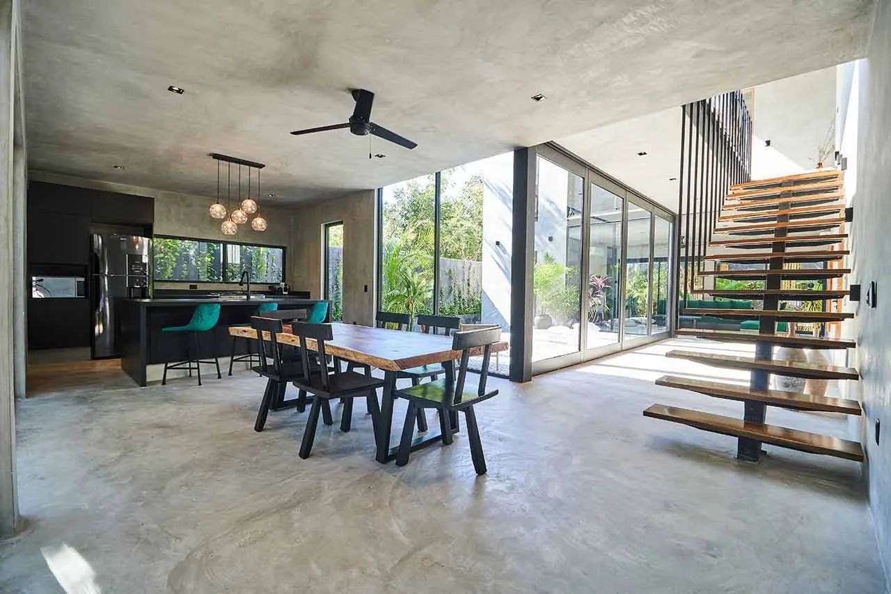Comedor de planta abierta con una mesa larga junto a la cocina y grandes ventanales.