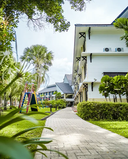 Representative hotel space: A paved walkway passes through landscaped grounds beside a white building.