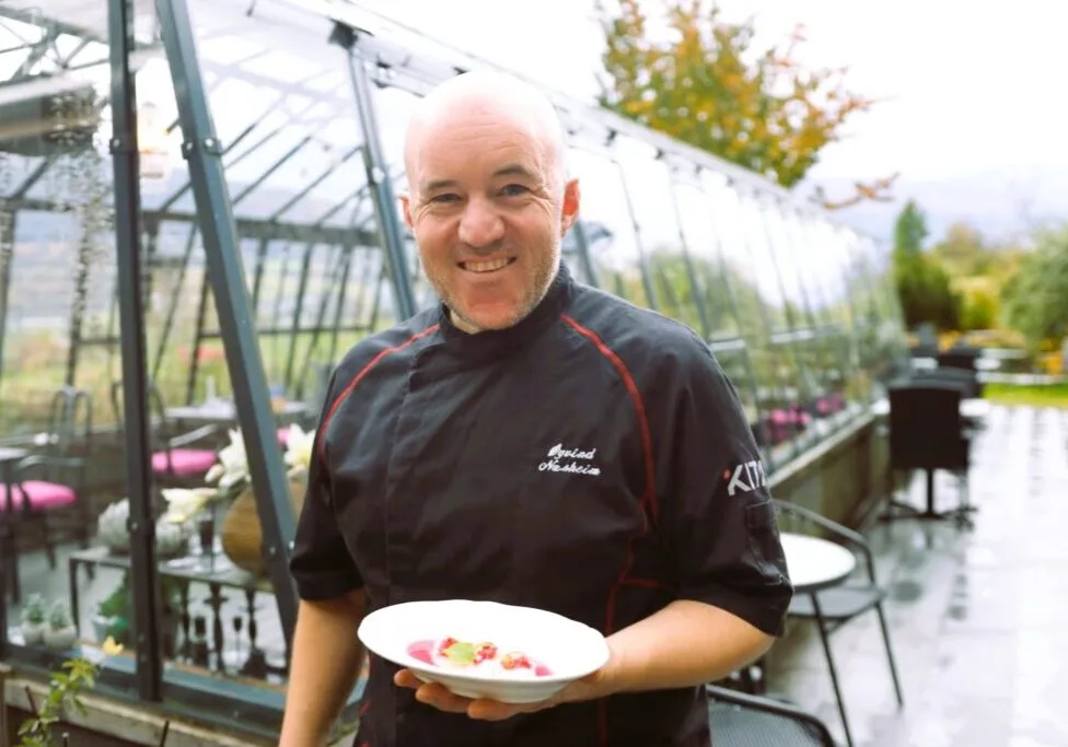 Representative hotel space: A chef holds a plated dish inside a glass greenhouse dining area.