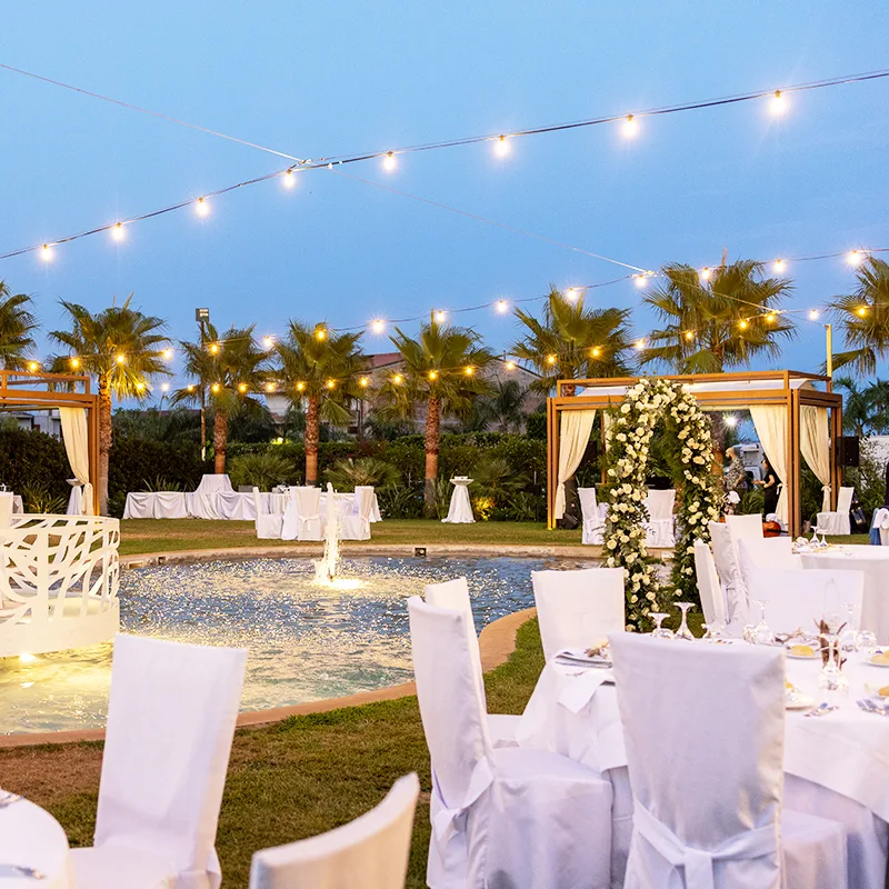 Representative hotel space: An outdoor event area has white dining tables beside a lit fountain and floral arch.