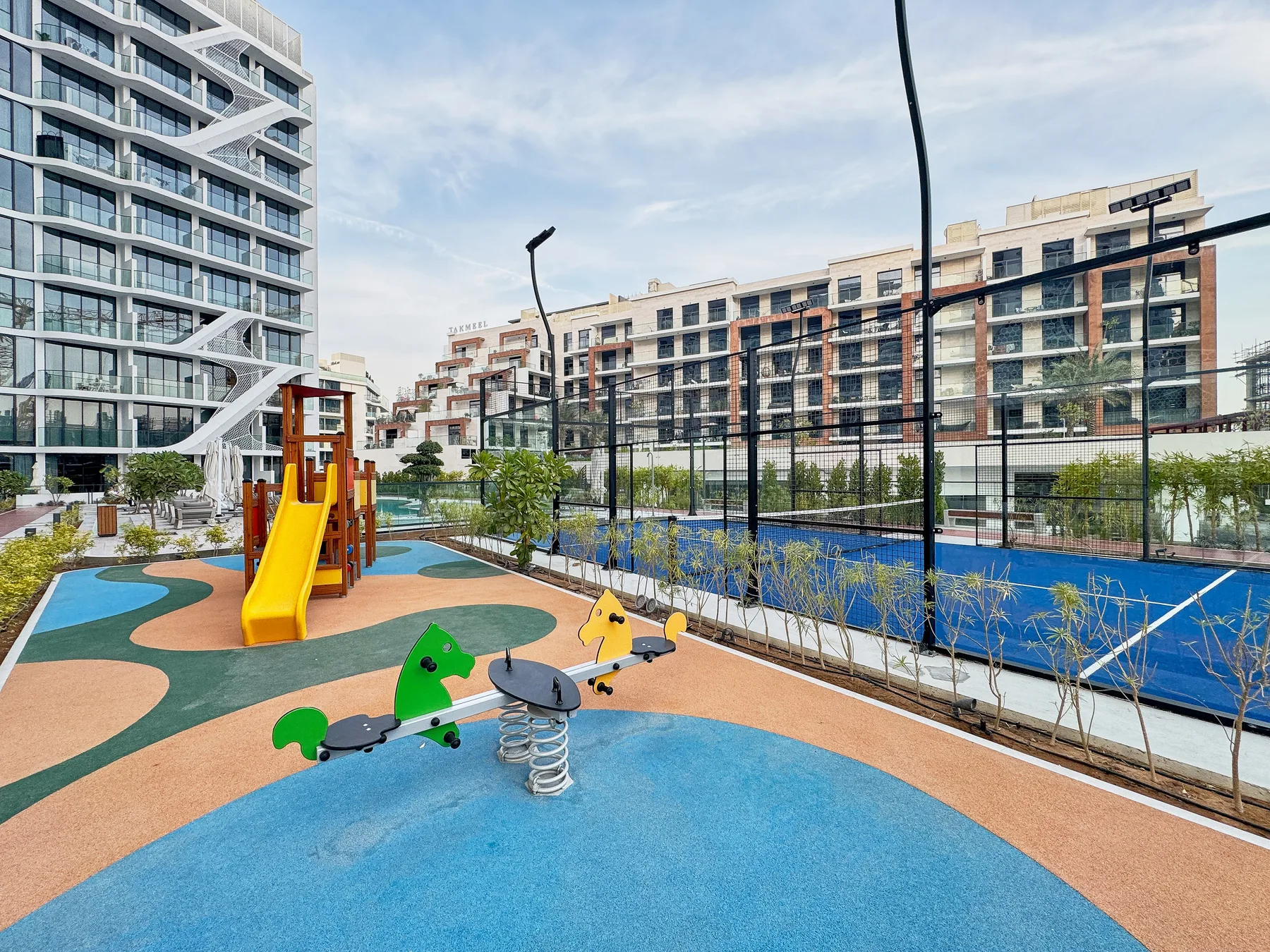 Shared amenity: An outdoor playground with colorful equipment beside a fenced sports court.