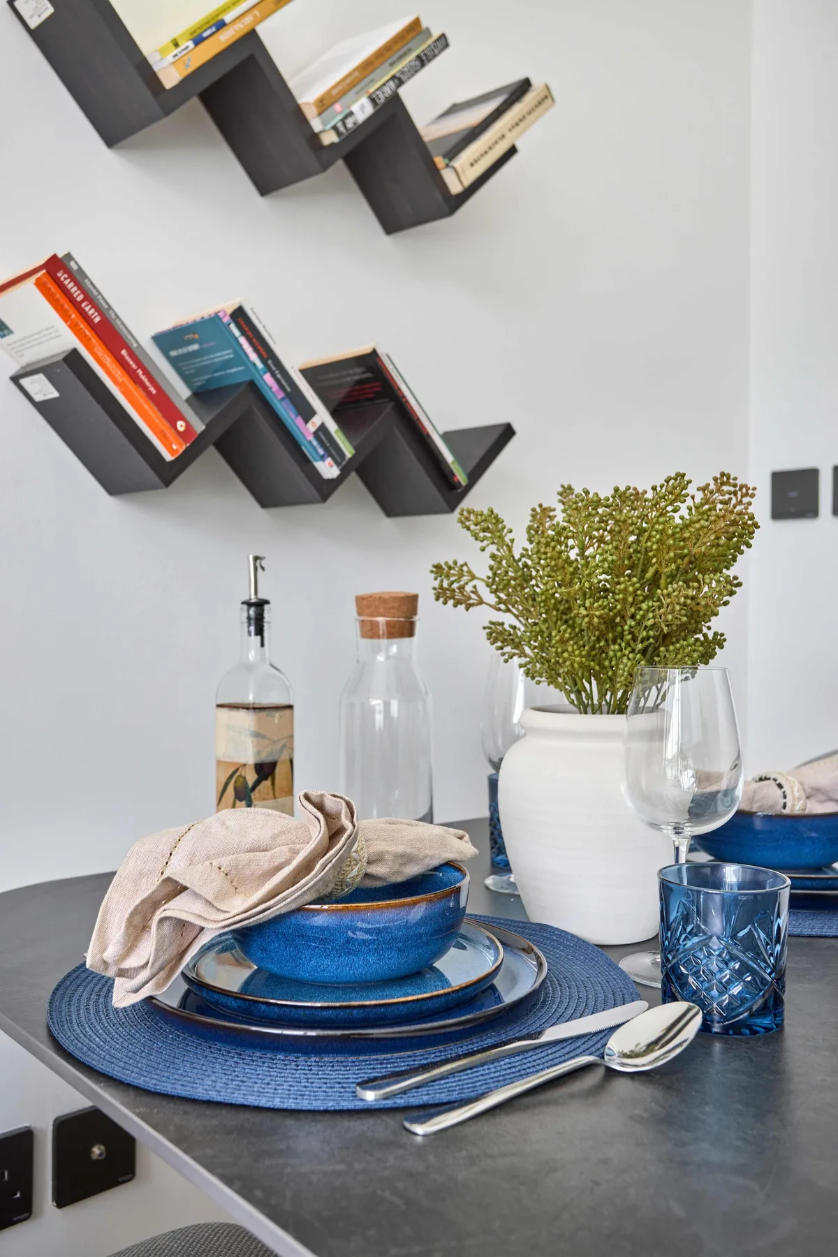 A dining table is set with blue plates, glasses, and a vase of flowers.