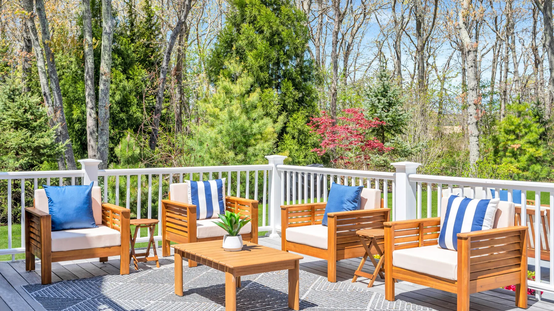 Outdoor deck seating with wooden lounge furniture and a view of trees.