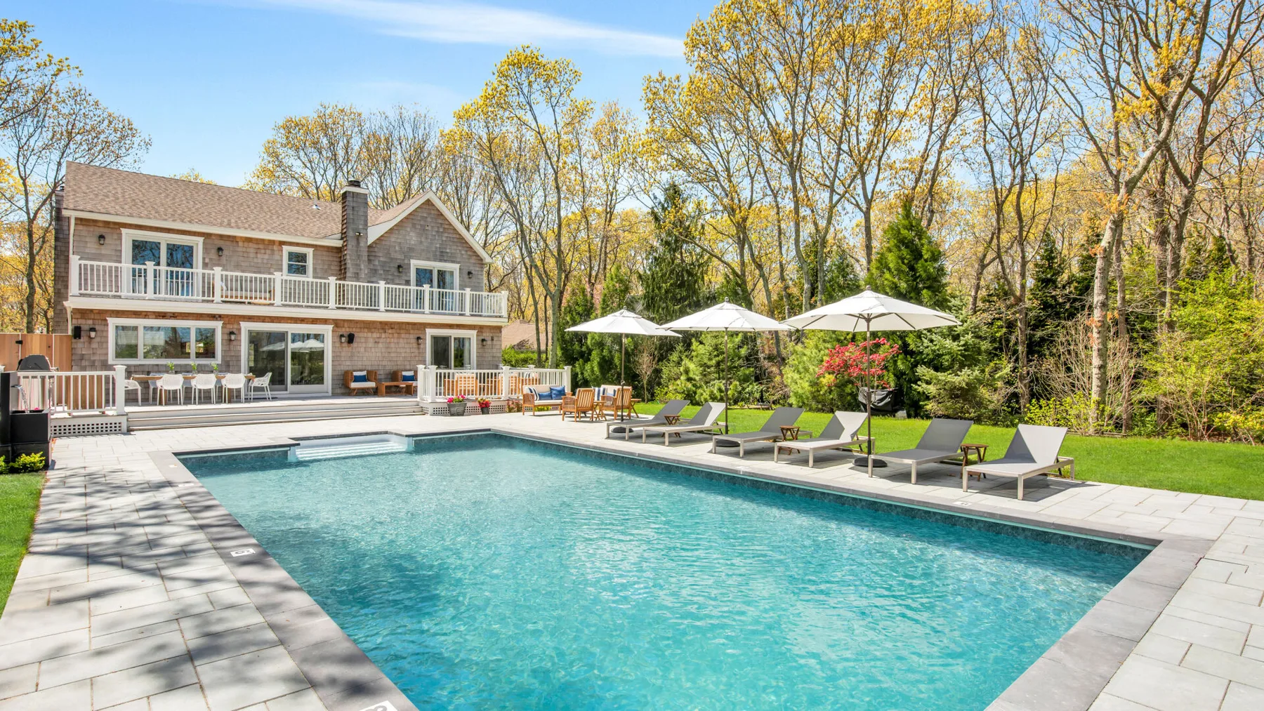An outdoor swimming pool beside a house, with lounge seating along the edge.