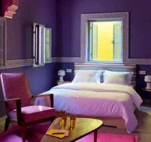 Espacio representativo del hotel: Un dormitorio con una cama, un sillón rojo tapizado y paredes moradas.