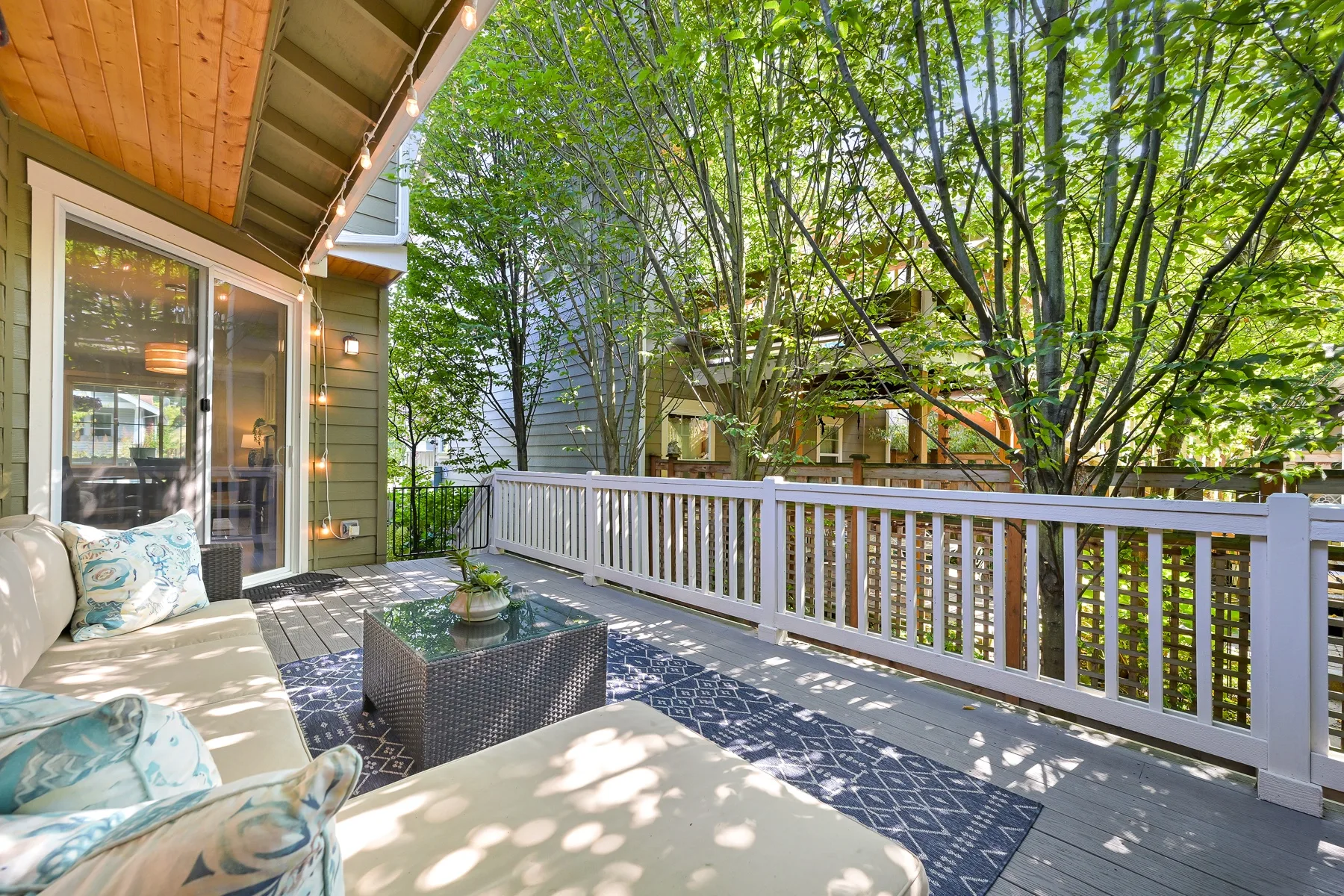 A furnished outdoor deck with cushioned seating and leafy trees beyond the railing.