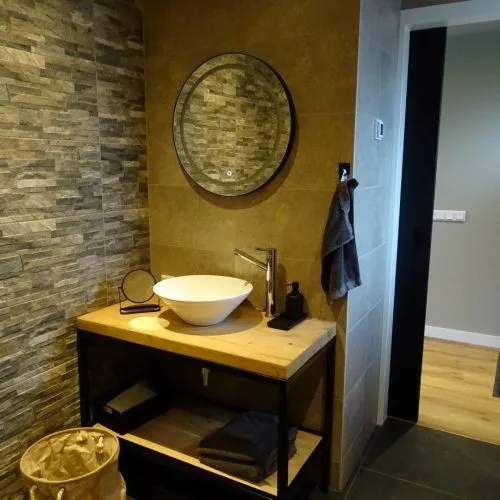 Espacio representativo del hotel: Un tocador de baño con lavabo sobre encimera y espejo redondo.