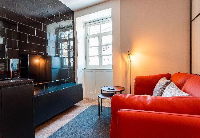 Una sala de estar con asientos rojos junto a una chimenea de azulejos oscuros.
