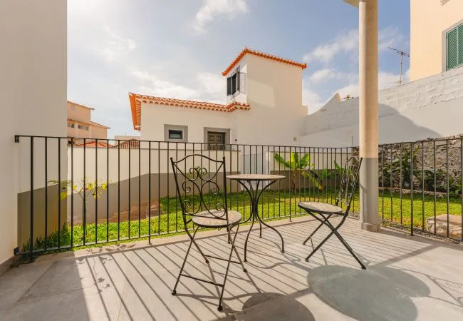 A sunny patio with metal seating overlooks a small garden.
