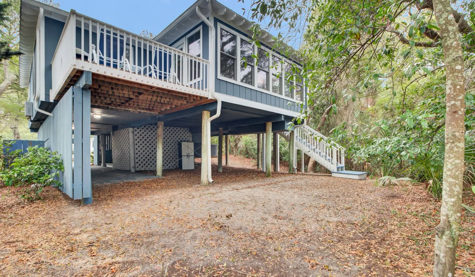 A raised house with a white-railed deck and stairs stands among trees.