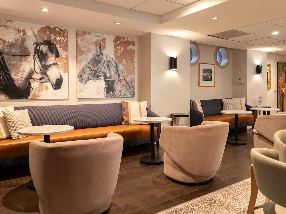 Representative hotel space: A hotel lounge with upholstered seating, small tables, and horse artwork on the walls.