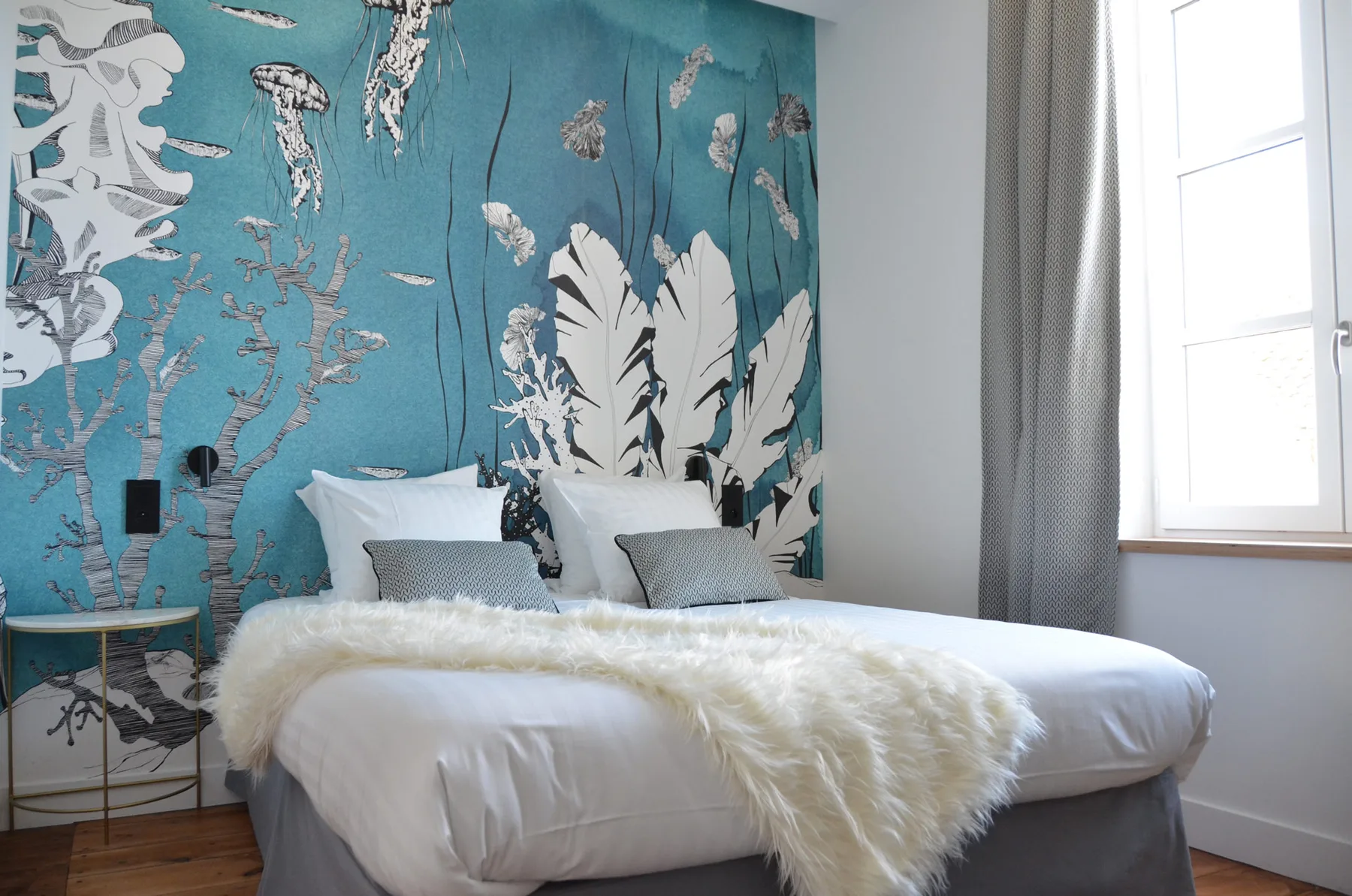 Representative hotel space: A bedroom with a bed dressed in white and a turquoise botanical mural.
