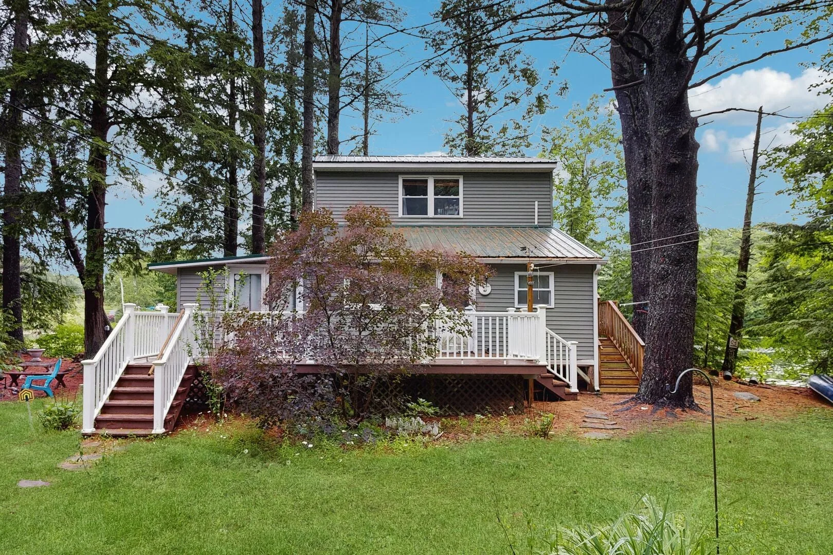 A gray house with a raised deck and white railings sits among trees.