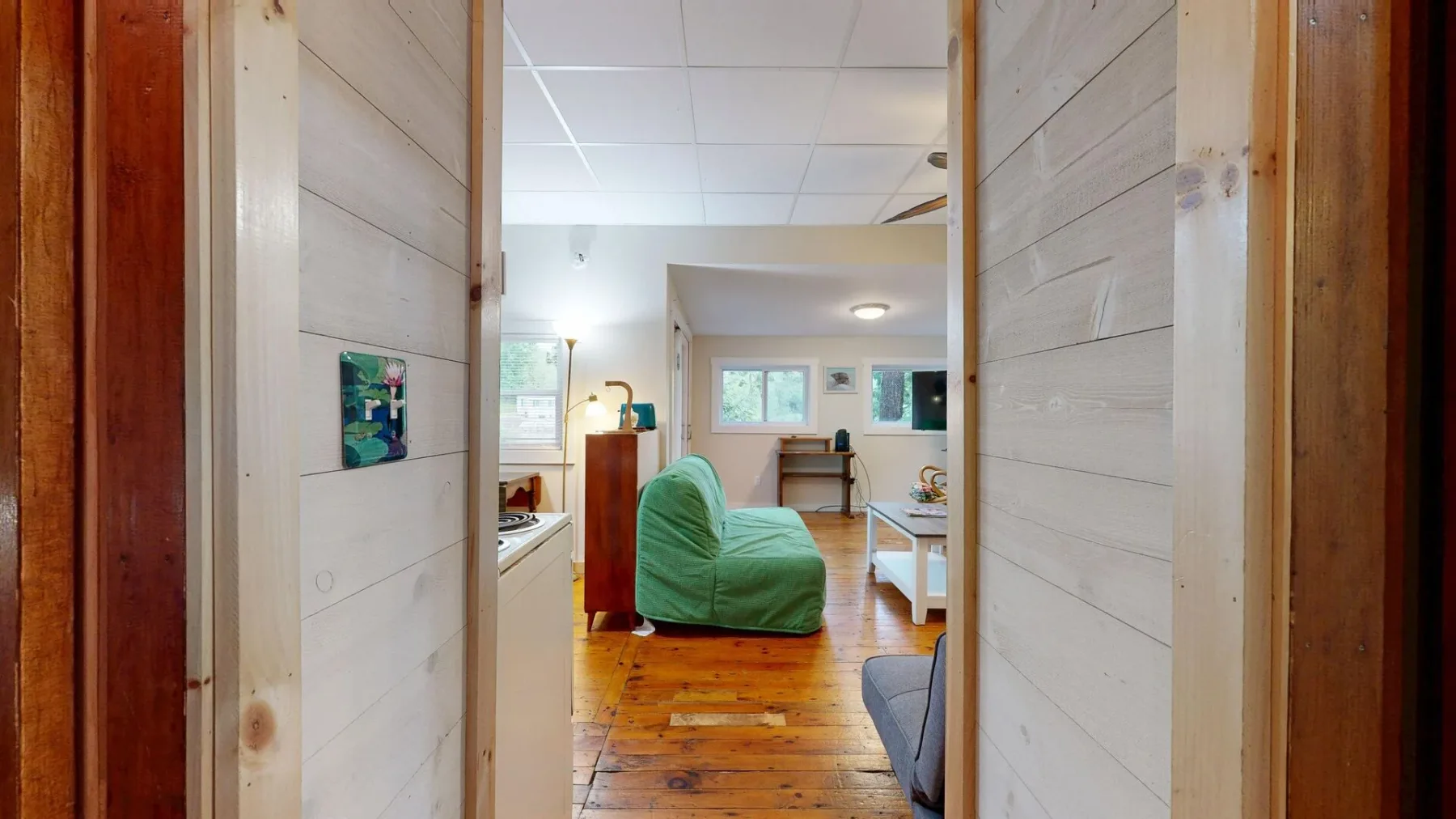 A living room with green seating and a wooden floor, viewed through an open doorway.