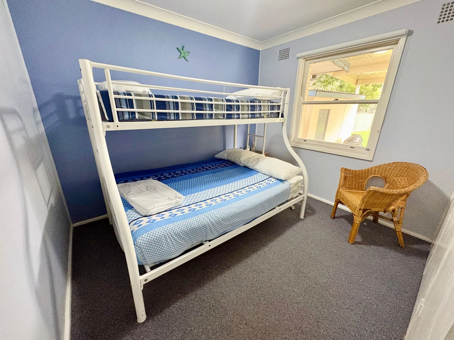 A small bedroom with a bunk bed and a wicker chair beside the window.