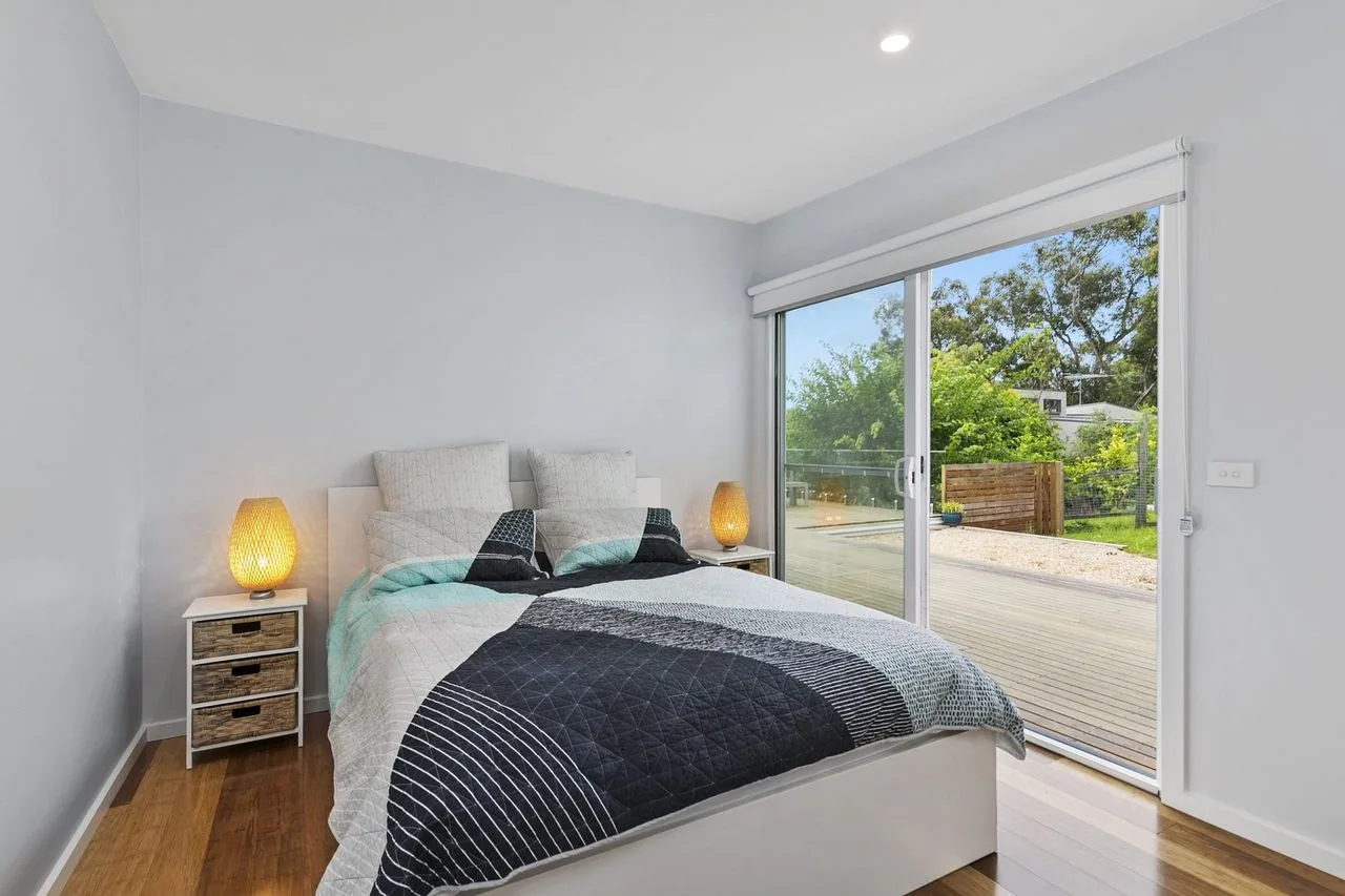 Un dormitorio luminoso con una cama junto a amplias puertas corredizas de vidrio.