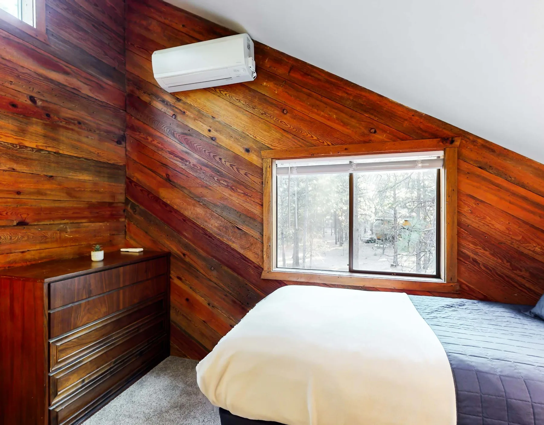 Un dormitorio con una cama bajo un techo inclinado revestido de madera y una ventana.