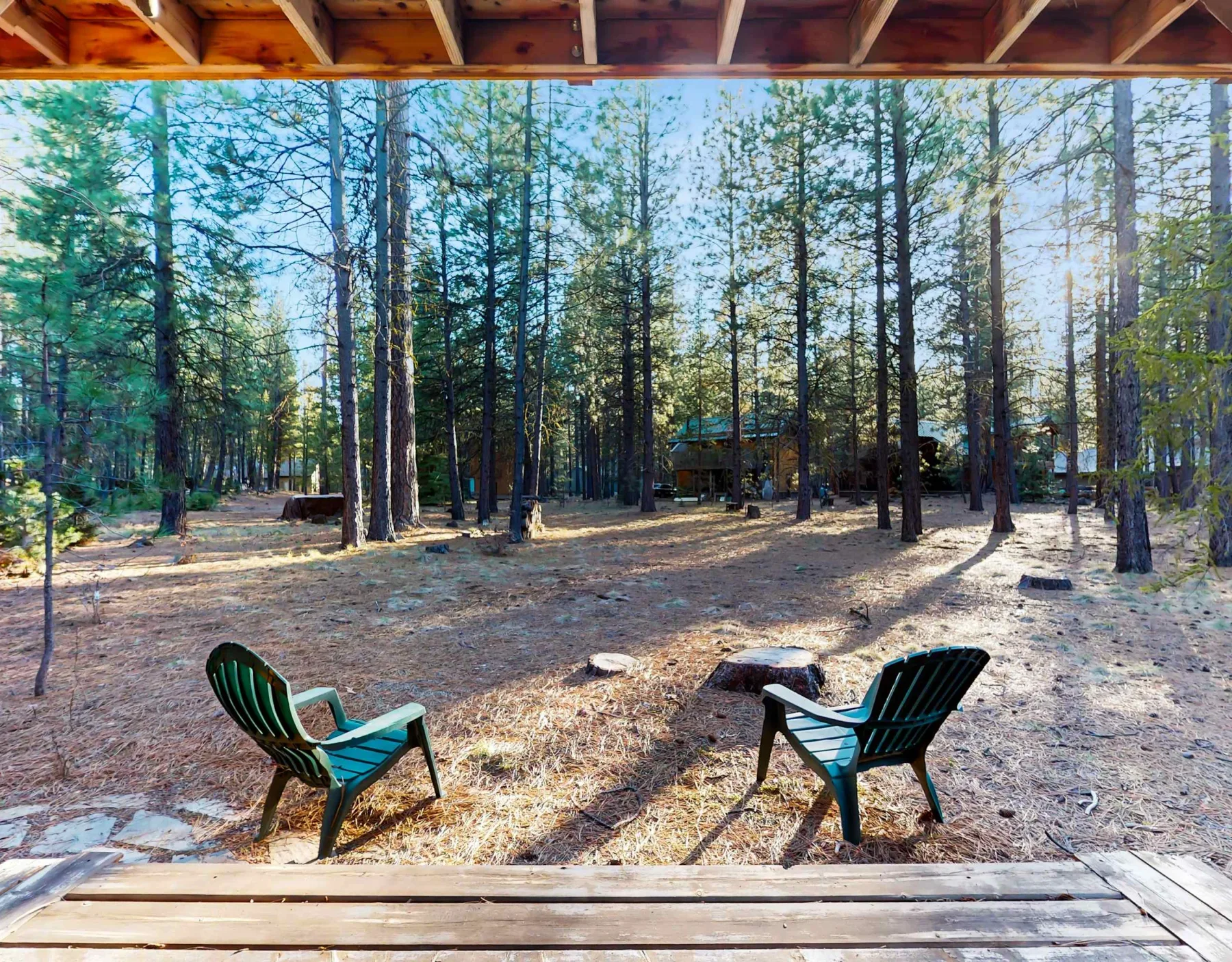 Zona de estar al aire libre entre árboles, con sillas bajo un alero de madera.