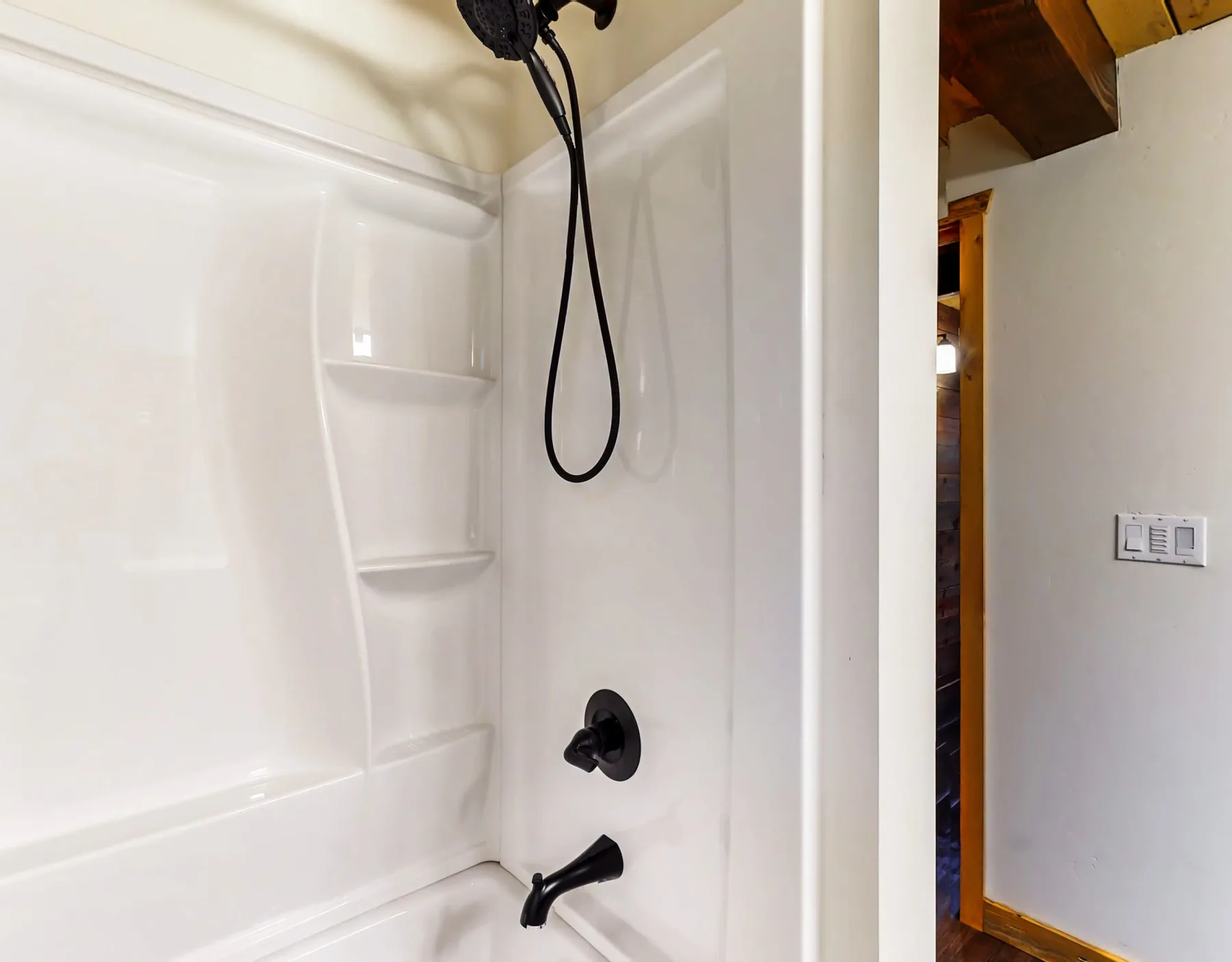 Una zona de ducha blanca tiene estantes esquineros integrados y accesorios oscuros.