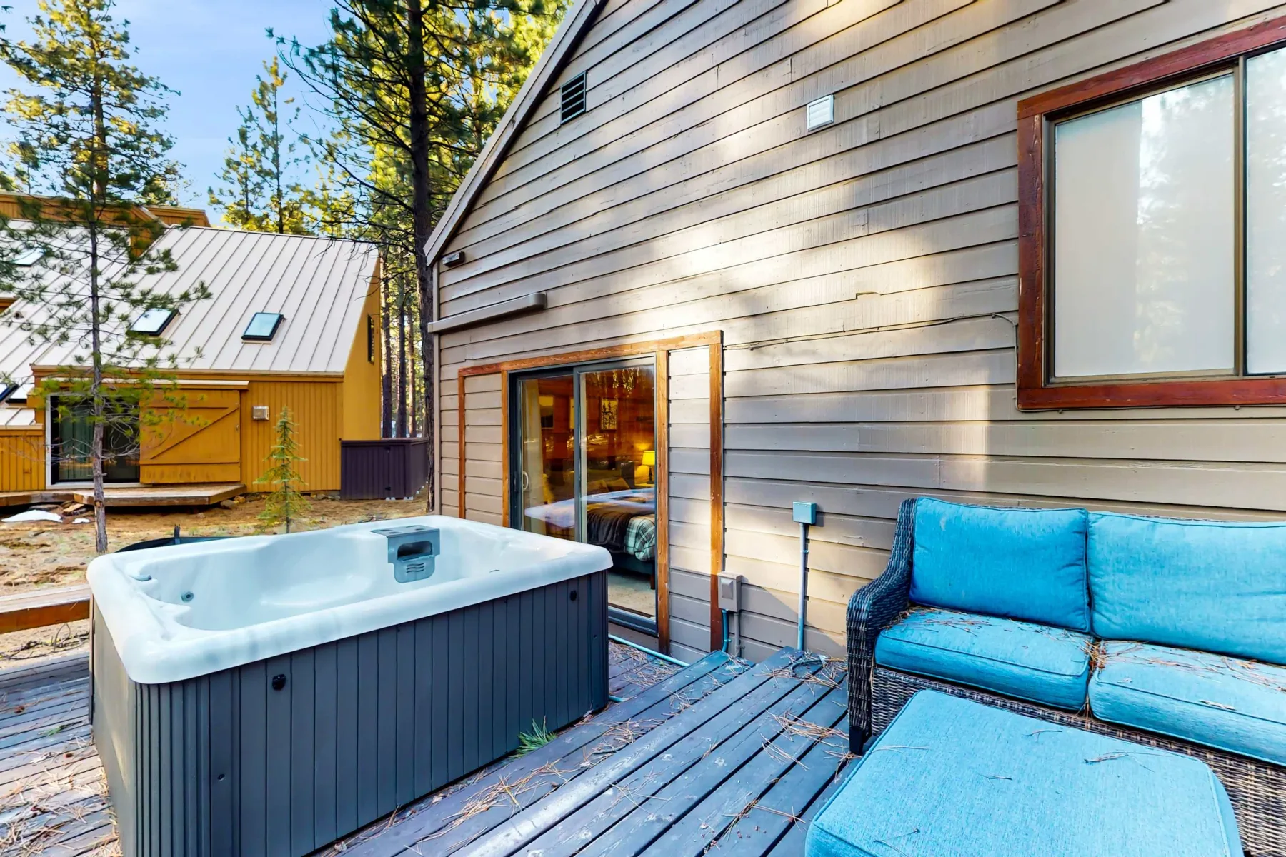 Una bañera de hidromasaje y asientos azules están en una terraza de madera junto a una cabaña.
