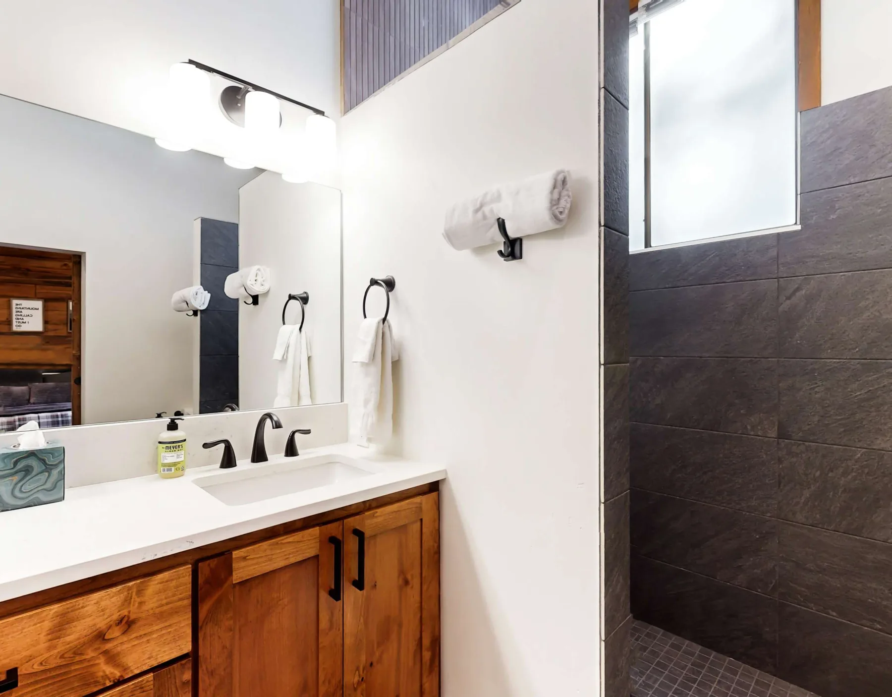 Un tocador de baño con espejo y una ducha al lado con azulejos.
