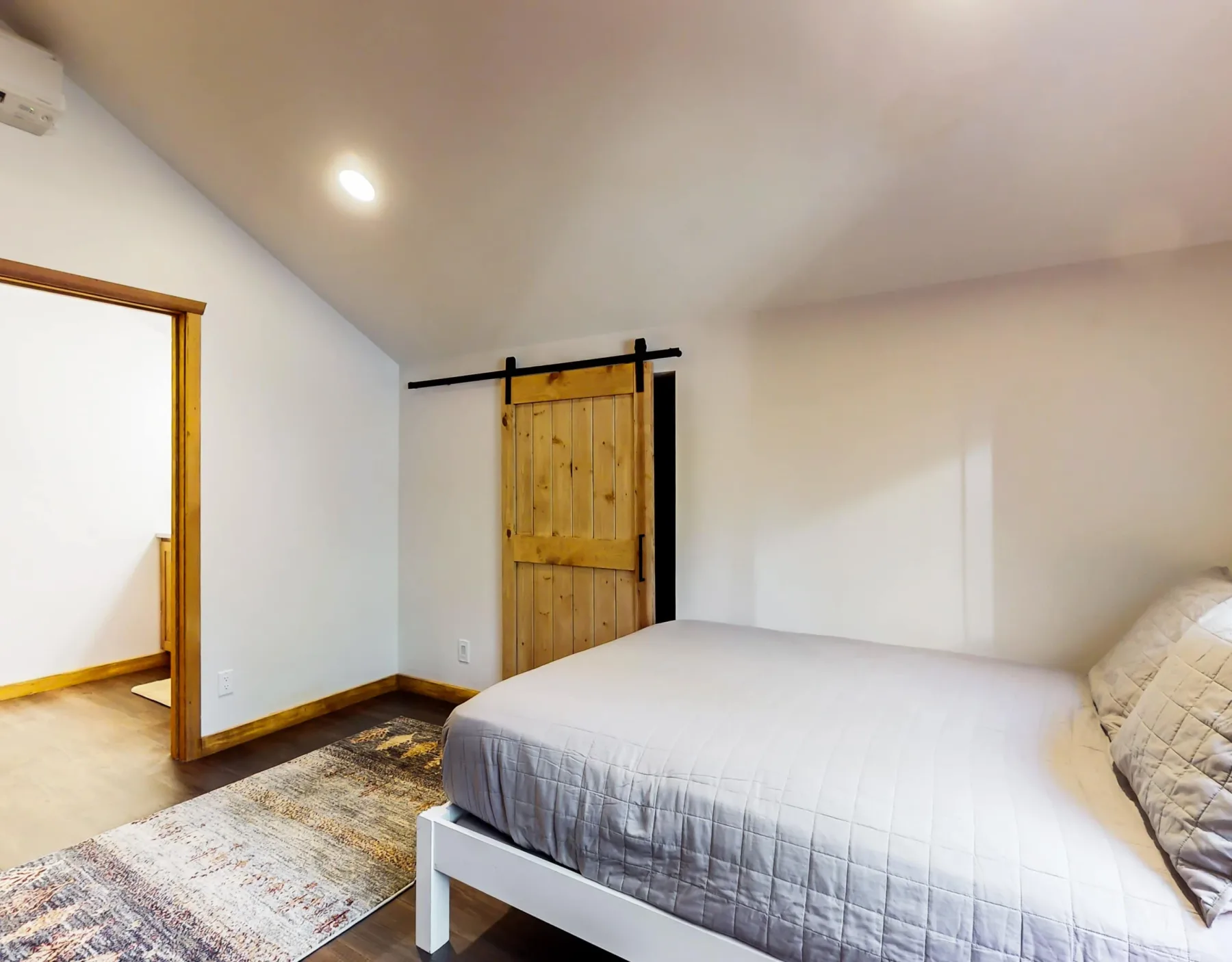 Un dormitorio con una cama, una puerta de madera y una alfombra estampada.