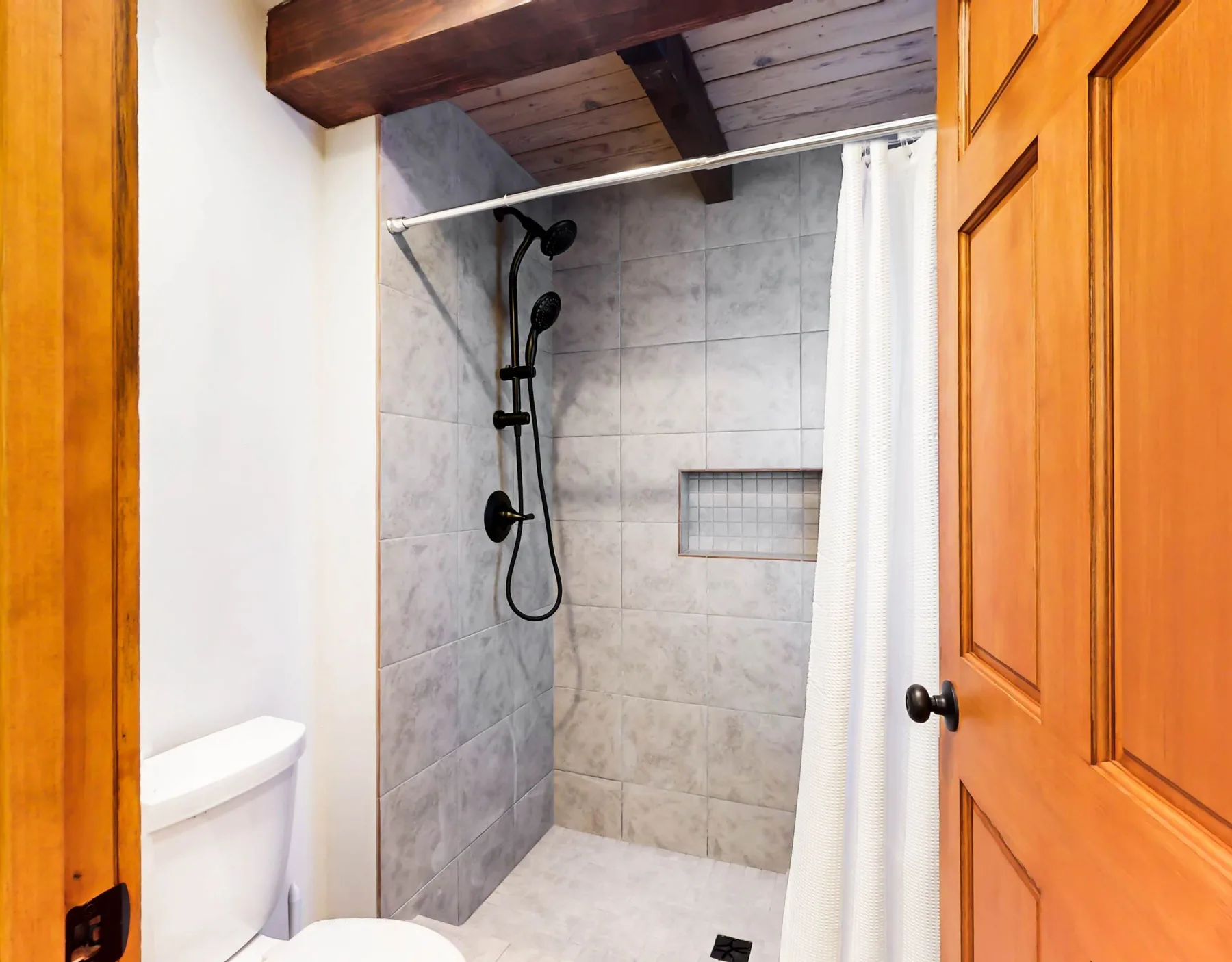 Un baño con ducha de azulejos, cortina blanca e inodoro.