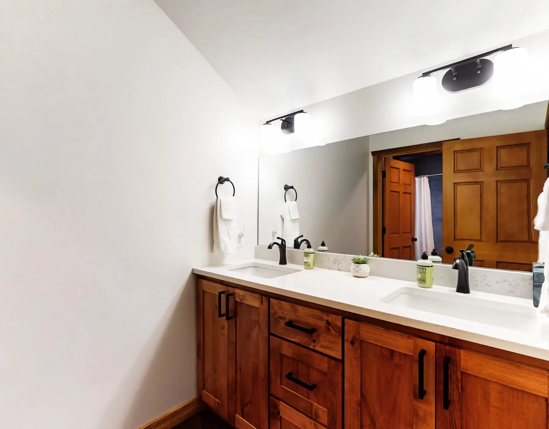 Un tocador de baño con un espejo amplio, luces brillantes y gabinetes de madera.
