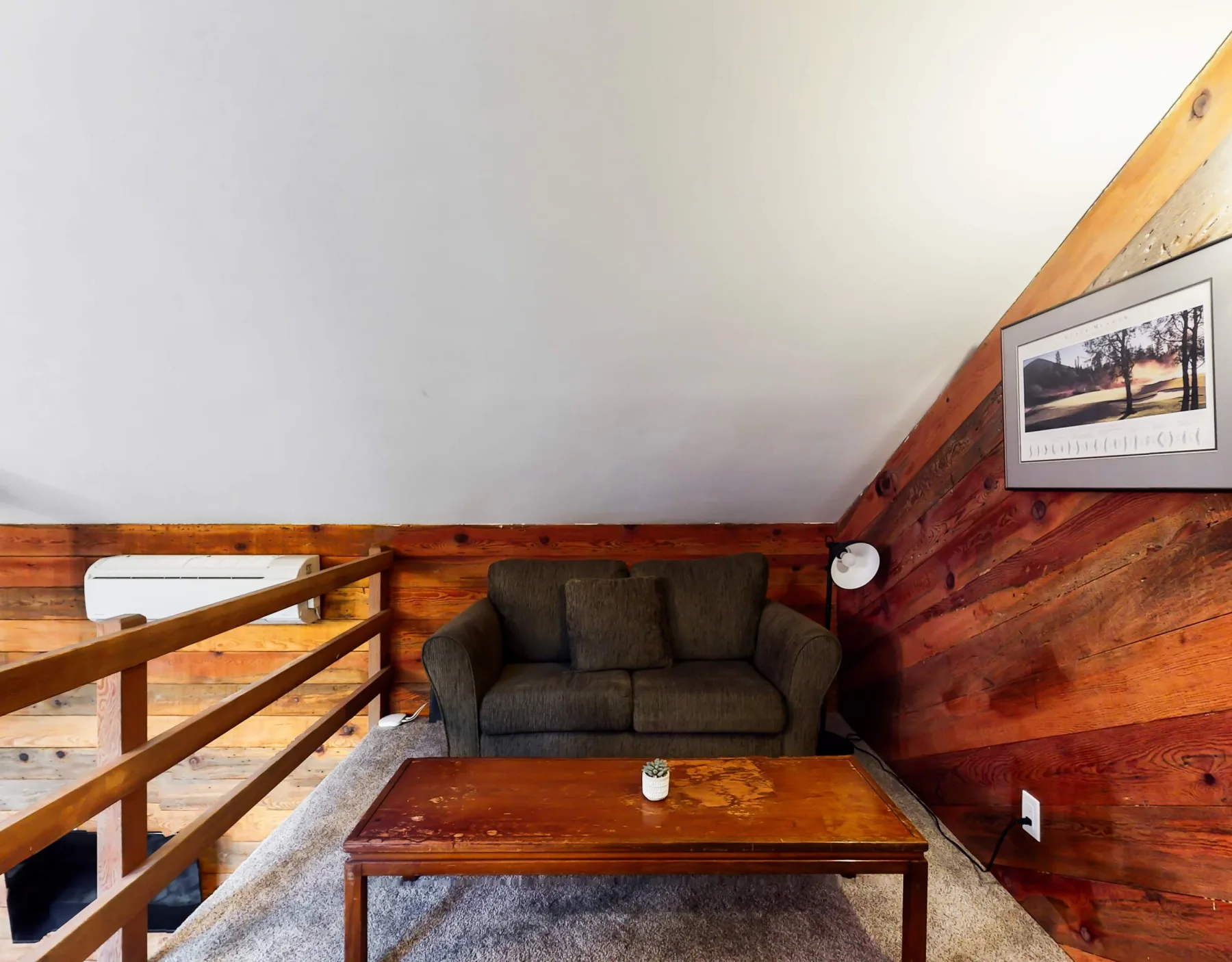Una acogedora sala en un altillo con un sofá oscuro y una mesa de centro de madera.
