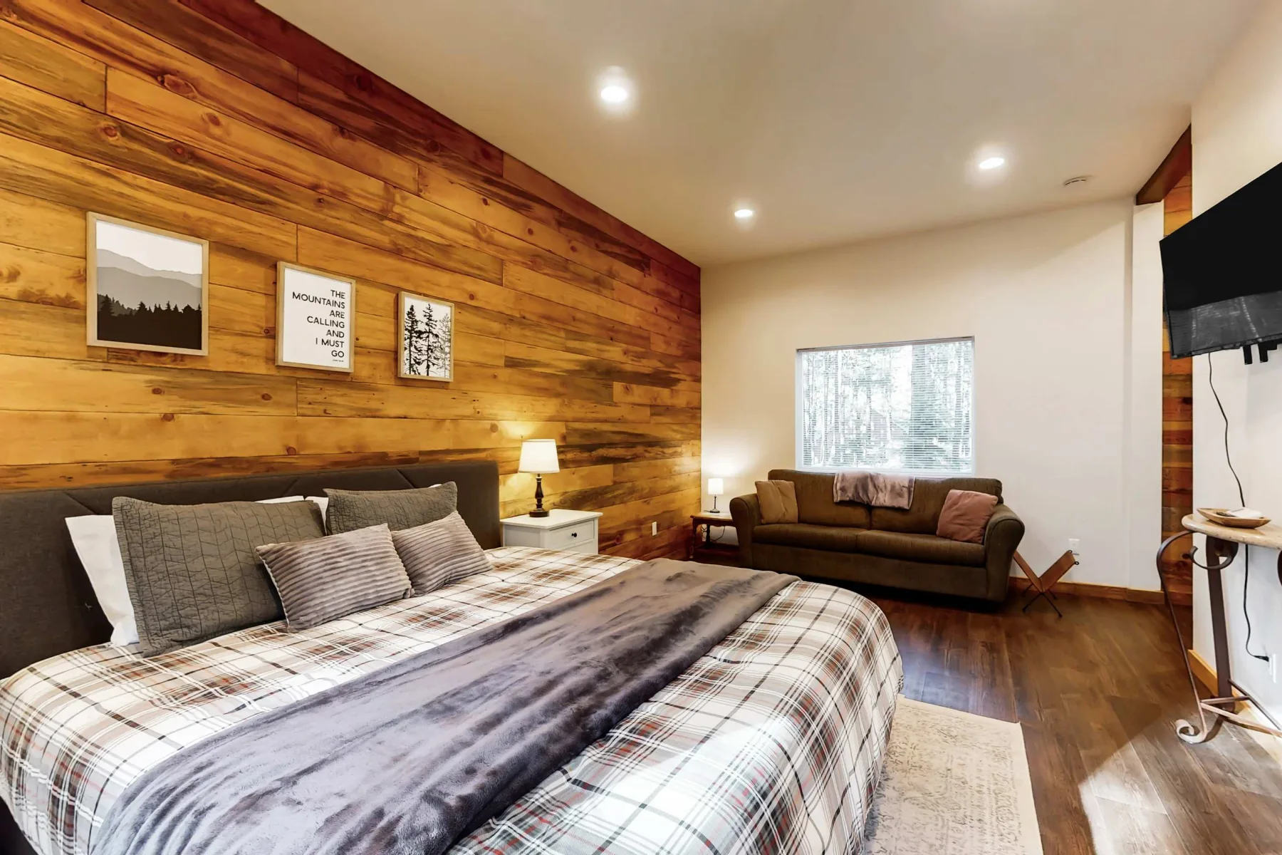 Dormitorio con una cama grande, una pared revestida de madera y asientos junto a la ventana.
