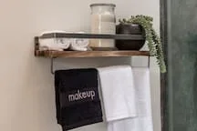 A bathroom towel rack holds folded towels beneath a shelf with toiletries.
