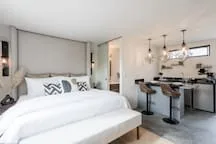 A bedroom with a bed and a kitchen area visible beyond it.