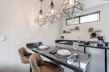 A dining area with a set table beneath geometric pendant lights.