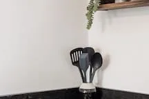 Kitchen utensils stand on a counter beneath a wall shelf.