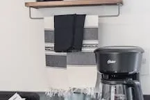 A kitchen counter with a coffee maker and dark cloth hanging from a shelf.