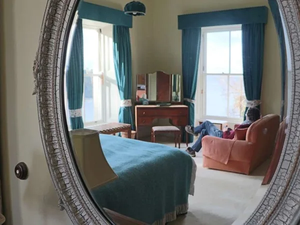Espacio representativo del hotel: Un dormitorio con cama, cómoda y sillón junto a dos ventanas.