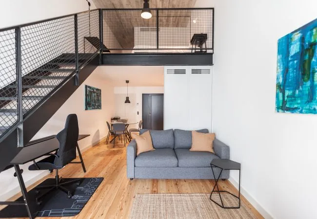 A loft living room with a gray sofa and an open metal staircase.