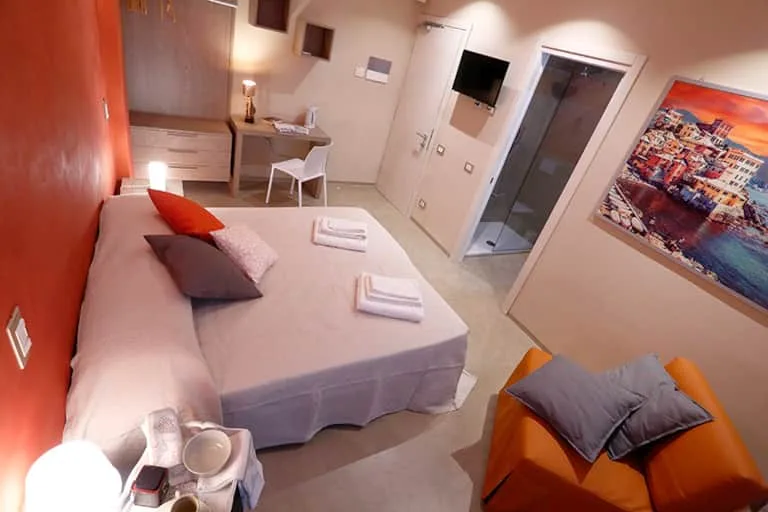 Espacio representativo del hotel: Dormitorio con una cama, un pequeño escritorio y una pared naranja.
