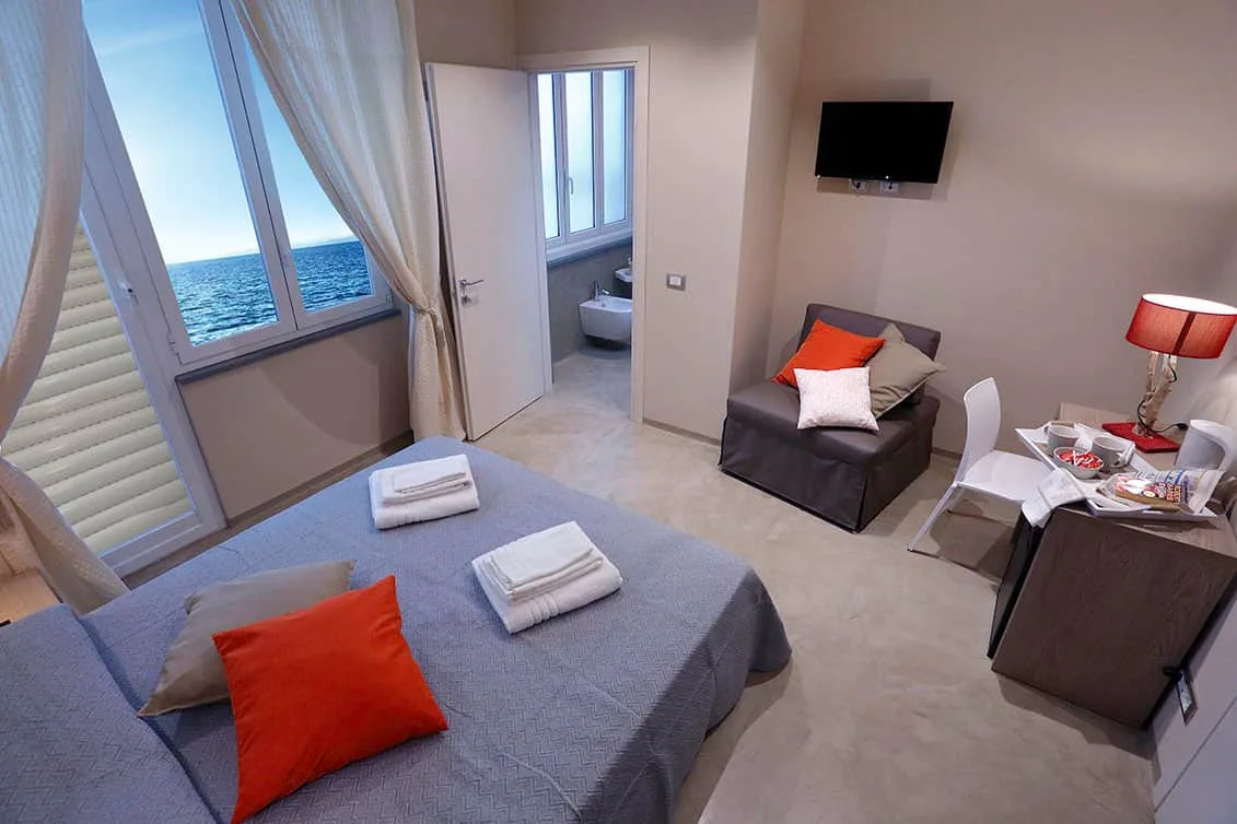 Espacio representativo del hotel: Una habitación con cama, asiento y una ventana con vistas al mar.
