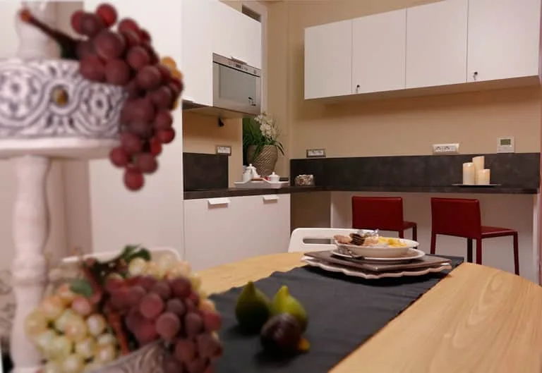 Espacio representativo del hotel: Una mesa de comedor está frente a una cocina con gabinetes blancos y sillas rojas.