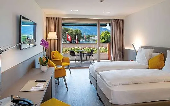 Espacio representativo del hotel: Una habitación de hotel con camas individuales, asientos amarillos y un balcón con vistas a la vegetación.