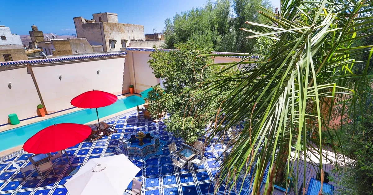 Espacio representativo del hotel: Una zona de piscina al aire libre con sombrillas rojas y suelo azul estampado.